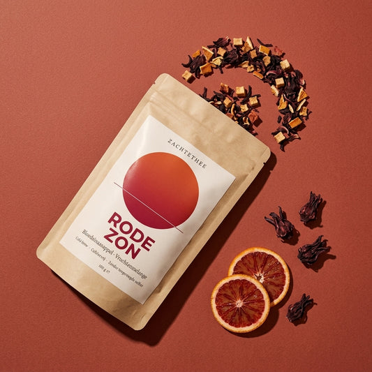 Rode Zon losse thee van bovenaf: doypack met uitgestrooide hibiscus, gedroogde sinaasappel en appelblokjes